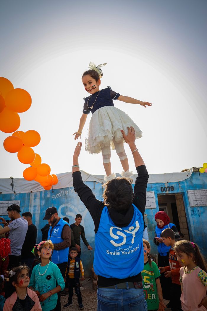 Children enjoying fun activities outdoors in Idlib, Syria, with balloons and festive atmosphere.