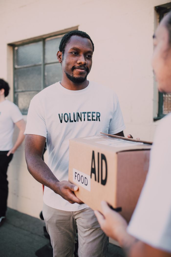 gallery-1 A volunteer hands a box labeled 'aid' and 'food' during an outdoor charity event.