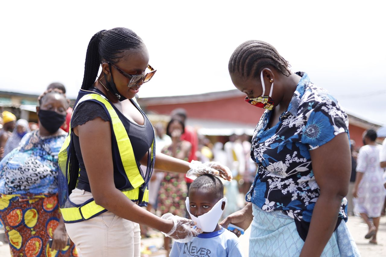 gallery-5 Women assisting a child with face mask in a community street setting.