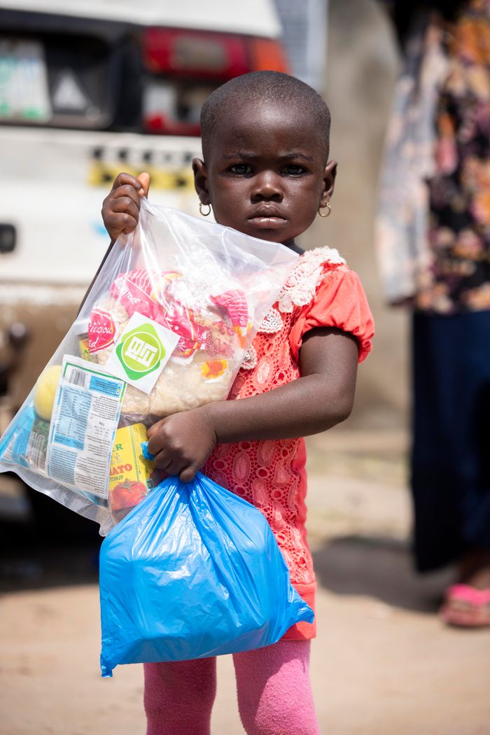 gallery-4 A young African girl holding relief supplies in plastic bags outdoors.